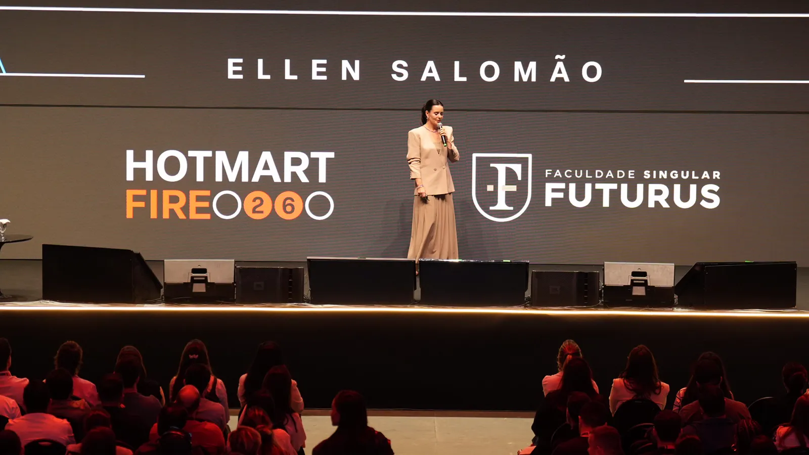 Ellen Salomão no palco do Hotmart FIRE 2026, com o nome dela no telão